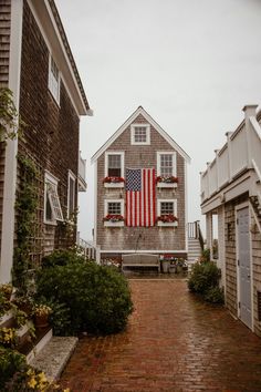 an american flag hanging from the side of a house on a brick walkway between two buildings