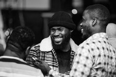 two men standing next to each other and one is looking at his phone while the other man smiles