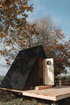 a small wooden structure sitting on top of a grass covered field next to a tree