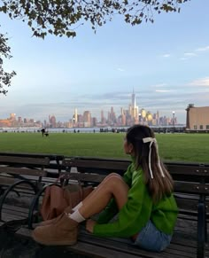 a woman sitting on top of a wooden bench in front of a cityscape