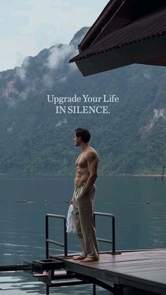 a shirtless man standing on a dock with mountains in the background