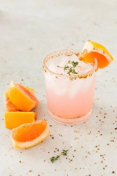 a pink cocktail with oranges and rosemary garnish on the rim next to it