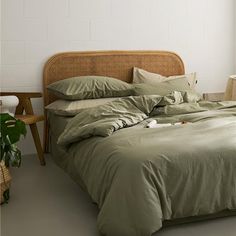 a bed with green sheets and pillows next to a potted plant in front of a window