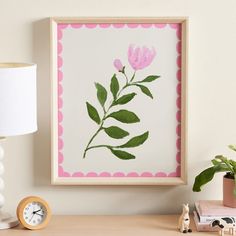 a pink flower is displayed in a frame on a desk next to a small clock