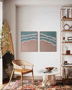 a living room with two paintings on the wall and a table in front of it