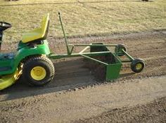 a green tractor pulling a trailer behind it down a dirt road next to a field