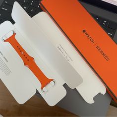 an orange apple watch in its packaging next to a laptop