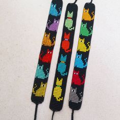 two cross - stitch bookmarks with different colored cats on them, one is black and the other is multicolored