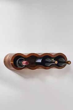 a wooden wine rack with three bottles in it on a white wall next to a bottle of wine