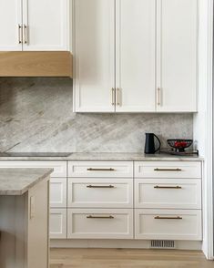 a kitchen with white cabinets and marble counter tops