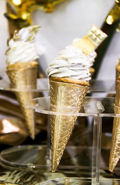 three ice cream cones with white icing and gold foil decorations on a clear plate