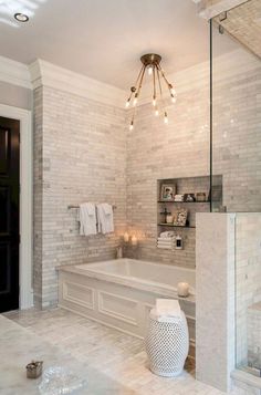 a large bathroom with white marble walls and flooring, lights above the bathtub