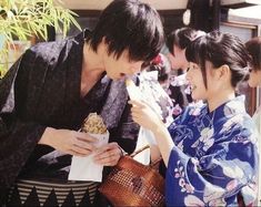 two women in kimonos are eating food from a paper bag and looking at each other