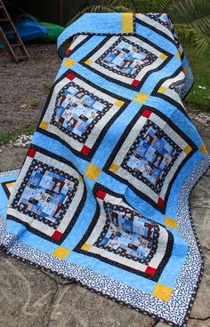 a blue and yellow quilt sitting on top of a cement ground next to a tree