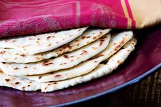 a purple plate topped with pita bread on top of a wooden table next to a red cloth