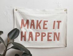 a white towel with the words make it happen printed on it next to a potted plant