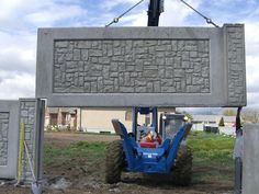 a man driving a small blue tractor in front of a cement sign