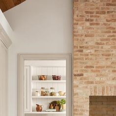 a brick fireplace in a kitchen with white cabinets and shelves filled with pots and pans