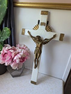 a crucifix with pink flowers and a potted plant in the corner