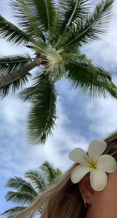 a woman's face with white flowers in front of palm trees and blue sky