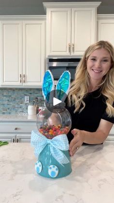 a woman sitting at a kitchen counter holding up a glass bowl with candy in it