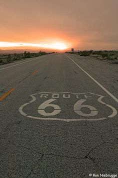 the sun is setting over an empty highway with a route 66 sign painted on it