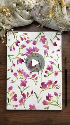 a card with watercolor flowers on it next to a pen and some dried flowers