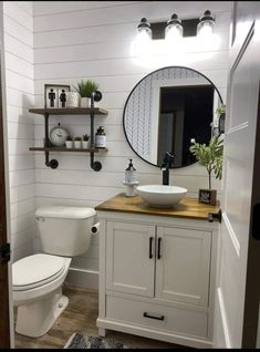 a white toilet sitting next to a sink in a bathroom under a round mirror above a wooden counter