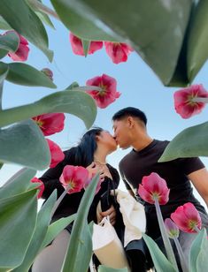 a man and woman kissing in front of pink flowers