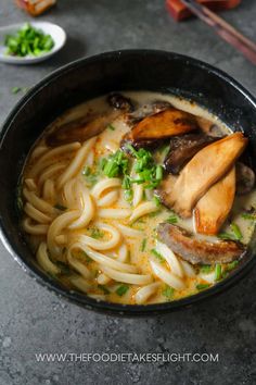 a close up of a bowl of food with noodles and meats in broth