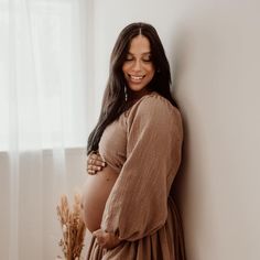 a pregnant woman leaning against a wall with her hands on her stomach and smiling at the camera