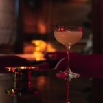 a wine glass sitting on top of a table next to a red chair and lamp