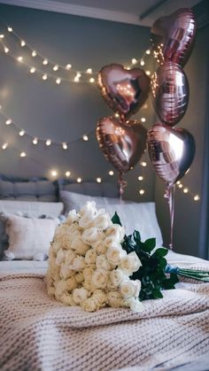 a bouquet of flowers sitting on top of a bed next to some foil heart balloons