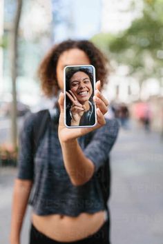 a woman taking a selfie with her cell phone in front of her face while walking down the street