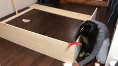 a woman kneeling down on the floor to build a bed frame