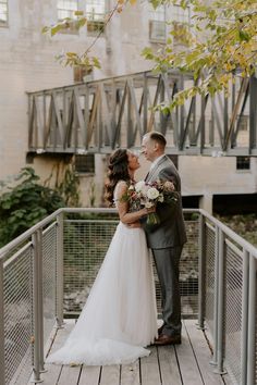 a bride and groom kissing on a bridge