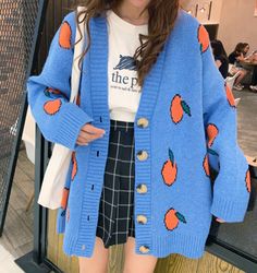 a woman wearing a blue cardigan with orange apples on it