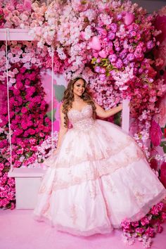 a woman in a pink dress posing for a photo with flowers on the wall behind her