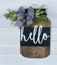 a wooden cutting board with the word hello painted on it and a black and white bow