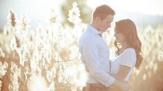 a man and woman standing next to each other in a field full of tall grass