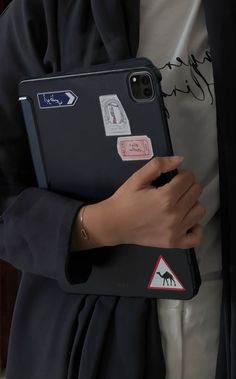 a person holding a black case with stickers on it and a phone in their hand