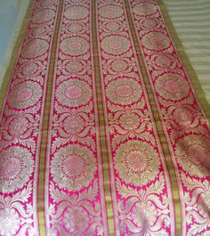 a pink and gold table runner on top of a white bed covered in sheets with intricate designs