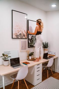 a woman standing on top of a desk in front of a laptop computer and painting