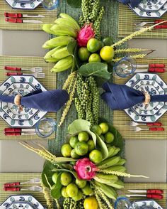 an arrangement of fruits and vegetables on a table with place settings in front of it