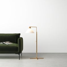 a green couch sitting next to a lamp on top of a wooden stand in front of a white wall