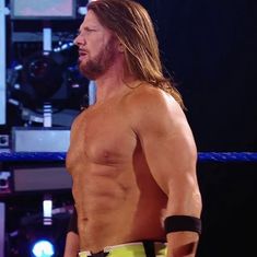 a man with long hair and no shirt standing in front of a ring holding a wrestling belt