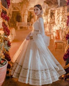 a woman in a white dress standing next to a flower covered archway with red and yellow flowers