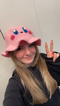 a woman wearing a pink crocheted hat making the peace sign with her hand