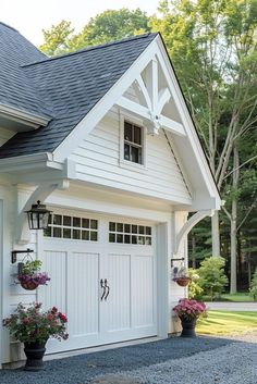 a white garage with flowers in the front and two potted plants on the side