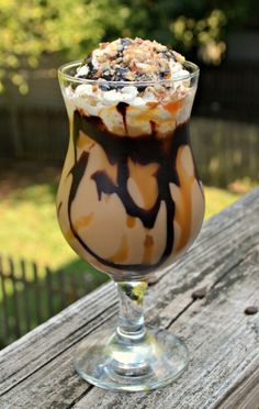 a glass filled with ice cream and chocolate on top of a wooden table next to a fence